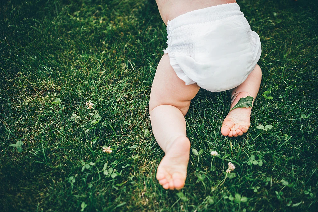 Baby wearing a white disposable diaper on green grass